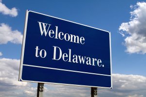 Welcome to Delaware sign on the state live against a cloudy blue sky.